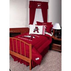 a bed with red sheets and pillows in a bedroom next to a lamp on a dresser