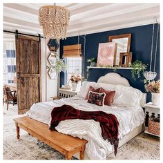 a bedroom with blue walls, white bedding and wooden accents on the ceiling is decorated with hanging plants