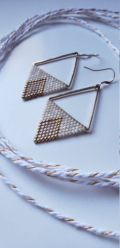 two pairs of earrings sitting on top of a white table next to some cords and rope