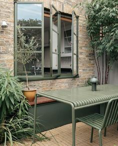 an outdoor table and chairs in front of a brick wall with potted plants next to it