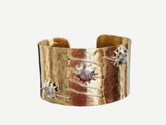 This cuff is 14K Gold Filled Metal that has been hammered to give it a Beautiful texture.  Sterling Silver wire is then weaved in and out with Three Sterling Silver Sunbursts in a diagonal Design.  The cuff itself measures 1 1/2 inches wide.   This will easily fit up to a 7 1/2 inch wrist.  This is a stunning piece and is sure to start a conversation!   Gift Box included.... Artisan Gold Cuff Bangle Bracelet, Artisan Gold Bangle Cuff Bracelet, Gold Wearable Art Jewelry For Festivals, Luxury Handmade Brass Bracelets, Handmade Fusion Style Metal Cuff Bracelet, Handmade Artisan Metal Cuff Bracelet, Handmade Metal Fusion Cuff Bracelet, Handmade Fusion Metal Cuff Bracelet, Adjustable Gold Cuff Bracelet In Fusion Style