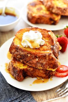 two white plates topped with french toast covered in butter and syrup next to strawberries