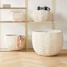 three white baskets sitting on top of a wooden floor next to a shelf filled with purses