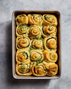 a baking pan filled with rolls covered in spinach and pesto on top of a gray surface