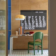 a green chair sitting in front of a desk with a calendar on the wall behind it