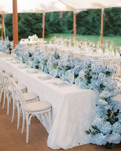 a long table with white chairs and blue hydrangeas is set up for a formal dinner