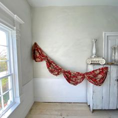 a room with white walls and wooden floors has red drapes hanging from the ceiling