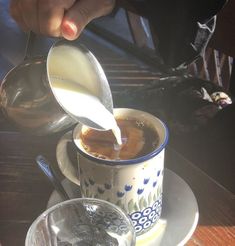 a person pouring milk into a cup on top of a plate next to a spoon