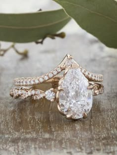 a pear shaped diamond ring on top of a piece of wood with leaves in the background