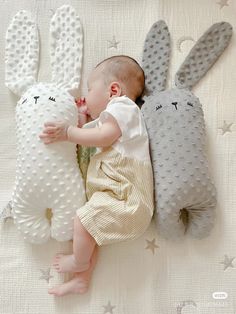 a baby laying on top of a bed next to two stuffed bunny rabbits and kissing each other