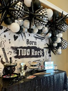 a table topped with black and white balloons next to a sign that says born two rock