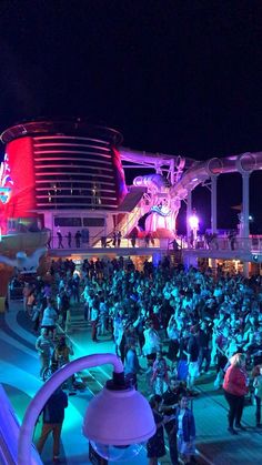 a large group of people standing around in front of a cruise ship at night time