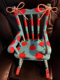 a wooden chair with red apples painted on the back and sides, tied to a cord