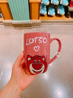 a hand holding a pink coffee mug with the words lotso on it and a smiling bear