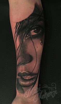 a woman's face with black hair and tears on her arm, done by tattoo artist