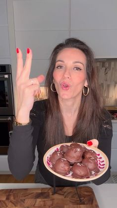 a woman holding a plate with chocolate covered doughnuts in front of her face