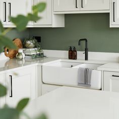 a kitchen with green walls and white cabinets, including a sink that has a black faucet