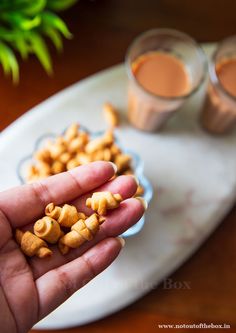 a person holding some food in their hand on a plate with two cups of coffee