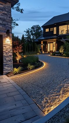 a house that is lit up at night with lights in the driveway and landscaping around it