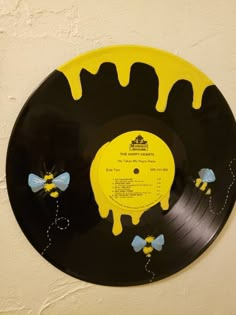 a yellow and black record with bees on it hanging from the wall in front of a white wall