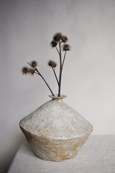 a white vase with three flowers in it sitting on a tableclothed surface next to a wall