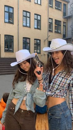 two women in cowboy hats are looking at their cell phones while standing next to each other