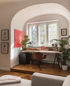 a room with a desk, chair and potted plants on the windows sill