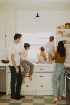 a group of people sitting on top of a kitchen counter next to each other in front of a window