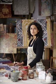 a woman standing in front of a table with art supplies on it and an easel behind her