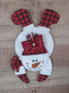 a snowman ornament hanging on the side of a wooden wall with red and black plaid fabric