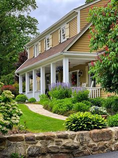 a house that is surrounded by flowers and plants in the front yard, with a stone walkway leading to it