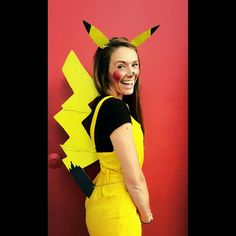 a woman in yellow overalls and black shirt standing next to a red wall with pokemon decorations on it