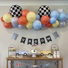 a birthday party with cars and balloons on the wall, including a race car cake table