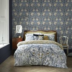 a bedroom with blue and white wallpaper, a bed covered in a comforter