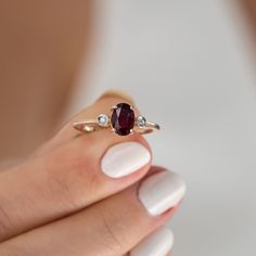 a woman's hand holding a ring with a red stone