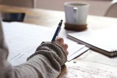 a person writing on a piece of paper at a table with a cup of coffee