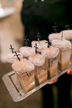 small desserts are arranged on a tray with tiny sticks sticking out of them and sprinkled with powdered sugar