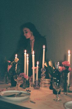 a woman sitting at a table with candles in front of her and plates on the table