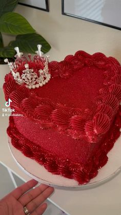 a heart shaped cake with a tiara on top is being held by a hand