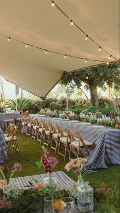 tables and chairs are set up under a tent for an outdoor wedding reception with lights strung from the ceiling