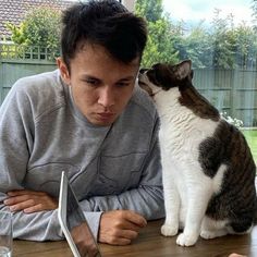 a man sitting at a table with a cat next to him looking at a laptop