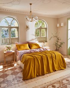 a bed with yellow sheets and pillows in a bedroom next to two large arched windows