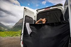 a man sitting in the back of a van drinking from a water bottle while camping