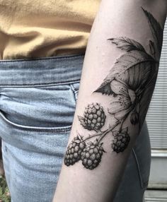 a woman with a tattoo on her arm holding a bunch of berries and leaves in front of her arm