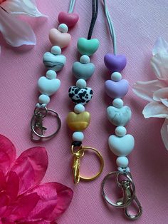 several different colored beads and keychains on a pink surface with flowers in the background