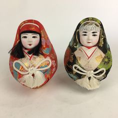 two dolls sitting next to each other on a white surface with one wearing a red headdress