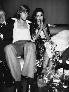 black and white photograph of three people sitting on a couch with drinks in front of them