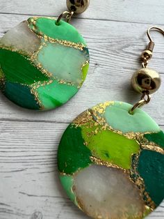 two green and gold earrings on top of a wooden table