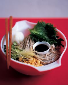 a bowl filled with noodles and vegetables next to chopsticks on a red table