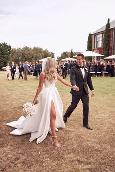 a bride and groom walking through the grass at their outdoor wedding in front of a large group of people